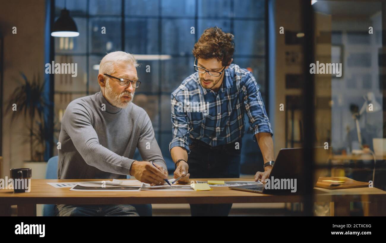 Chief Creative Designer Discusses Design Sheets with Young Developer. Two Professionals Having Discussion, Working with Documents, Choosing Right Stock Photo