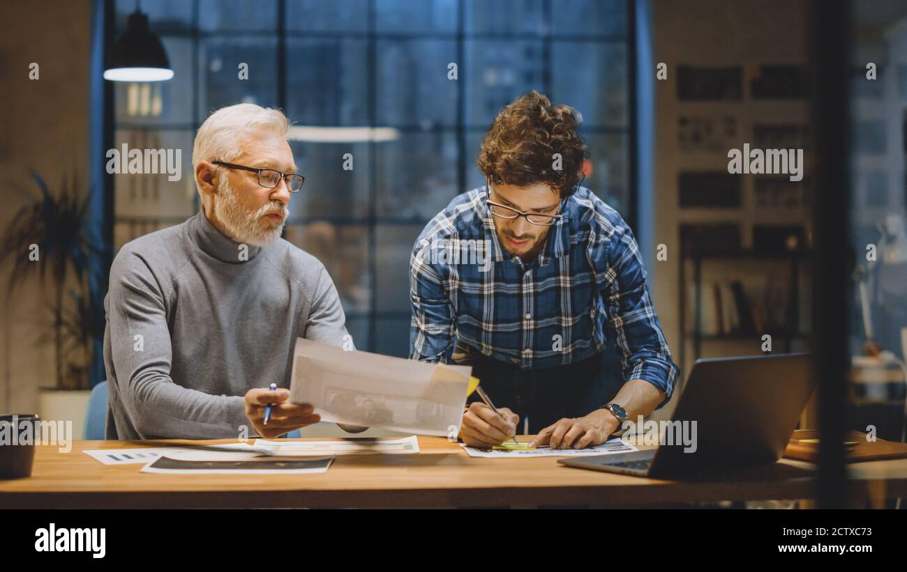 Chief Creative Designer Discusses Design Sheets with Young Developer. Two Professionals Having Discussion, Working with Documents, Choosing Right Stock Photo