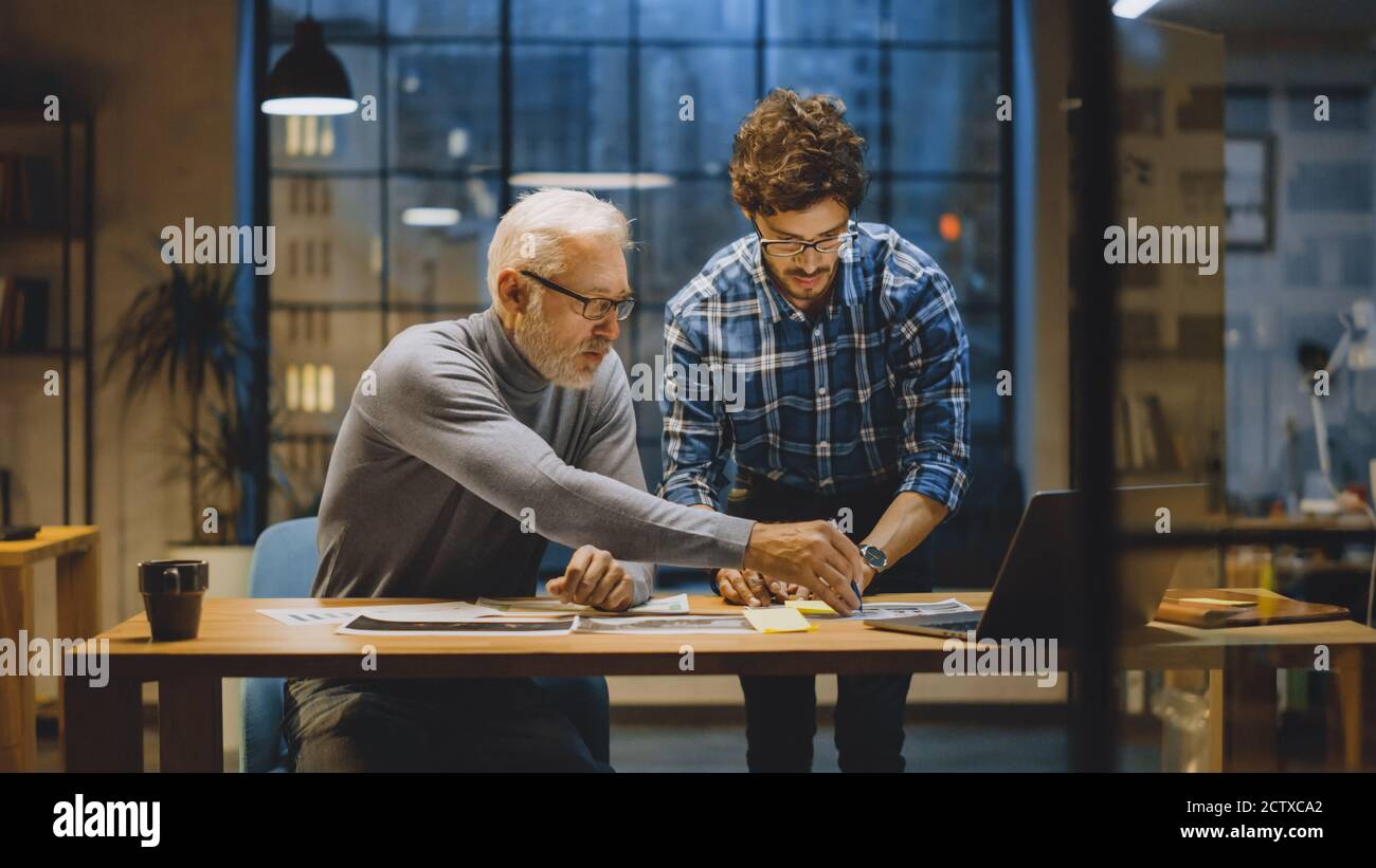 Chief Creative Designer Discusses Design Sheets with Young Developer. Two Professionals Having Discussion, Working with Documents, Choosing Right Stock Photo