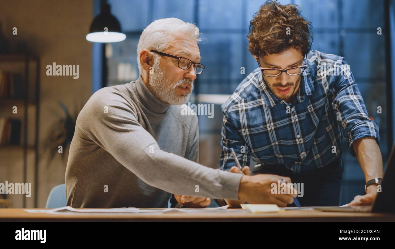 Chief Creative Designer Discusses Design Sheets with Young Developer. Two Professionals Having Discussion, Working with Documents, Choosing Right Stock Photo