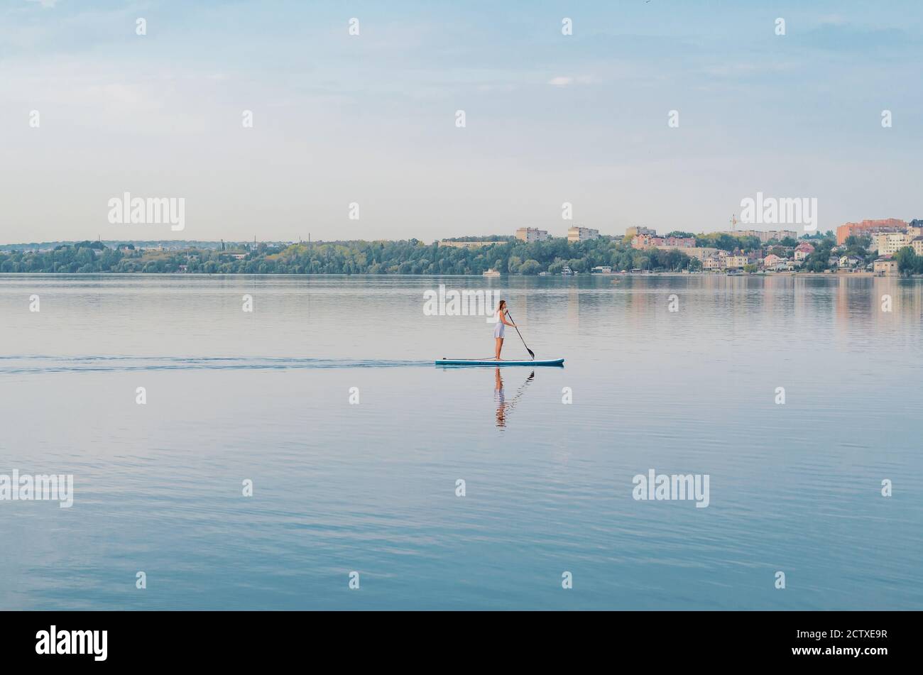 Young woman in a dress swims on the lake on surfboard Stock Photo