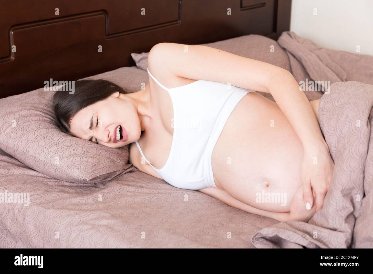 Stressed pregnant woman lying in bed with her hand on her stomach, grimacing from the bolt. Stock Photo