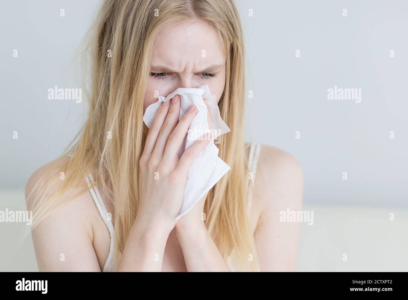 Sick young woman with a cold blowing her nose into a tissue paper at home. Close-up. Stock Photo