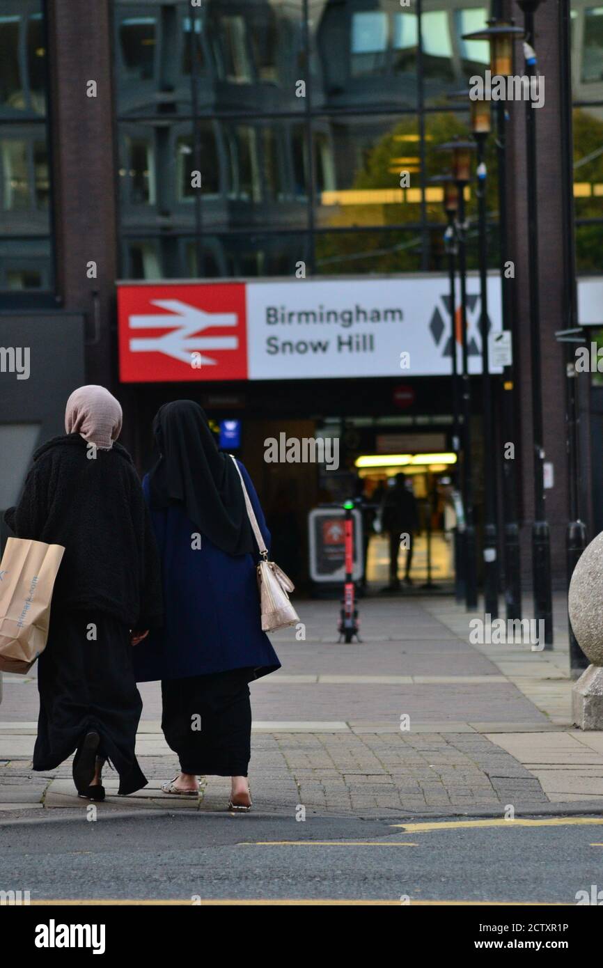 Two women in Islamic head-dress walk towards Birmingham Snow Street station, Voi electric scooters in the background Stock Photo
