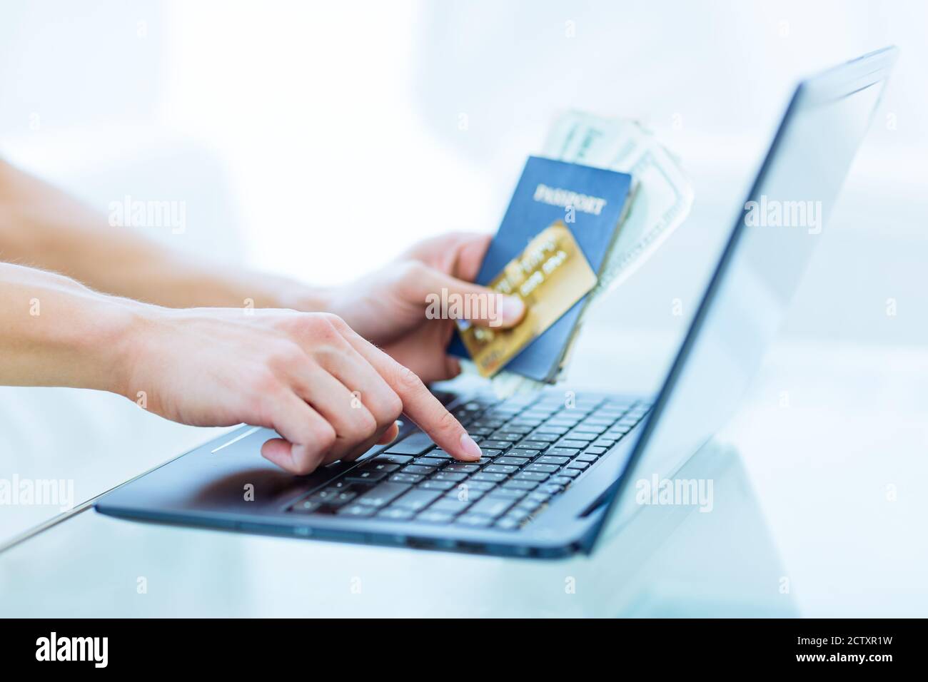 Online travel booking. Person's hands holding a passport, credit card and cash while using a laptop computer. Closeup. Stock Photo