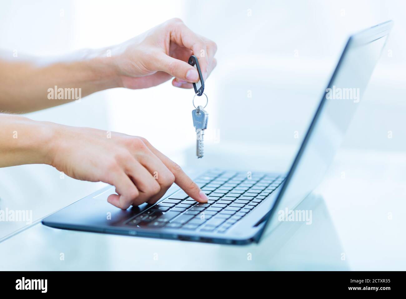 Person holding keys up while using a laptop computer. Online rental booking service. Closeup. Stock Photo