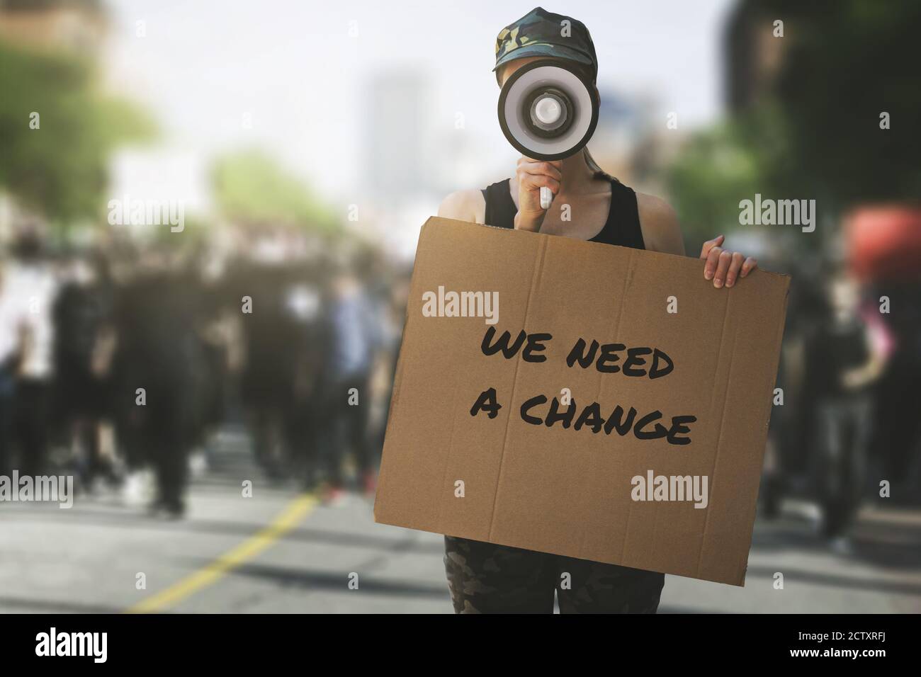 public protest and riots in the city streets. woman with megaphone and cardboard poster in hands on protesters crowd background. democracy concept Stock Photo