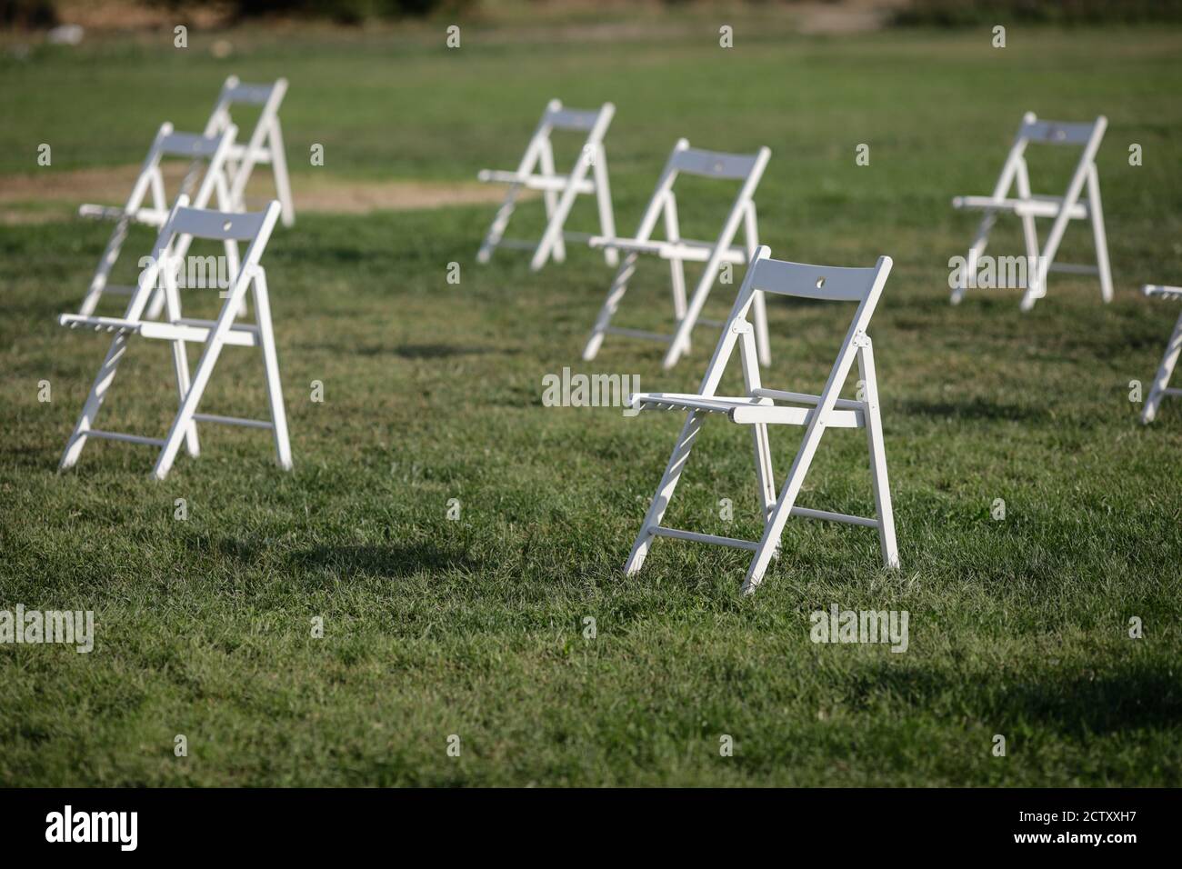 Chairs apart one from another to maintain the social distance during the Covid-19 outbreak at an outdoor event on the grass Stock Photo