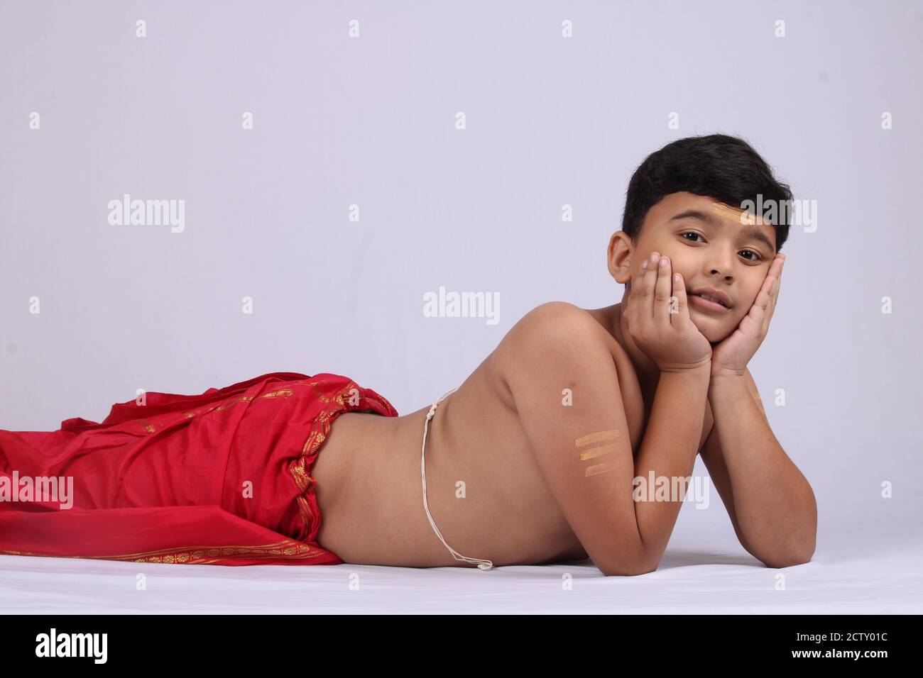 Young Indian boy in ethnic wear laying or enjoying leisure time over white background. Stock Photo