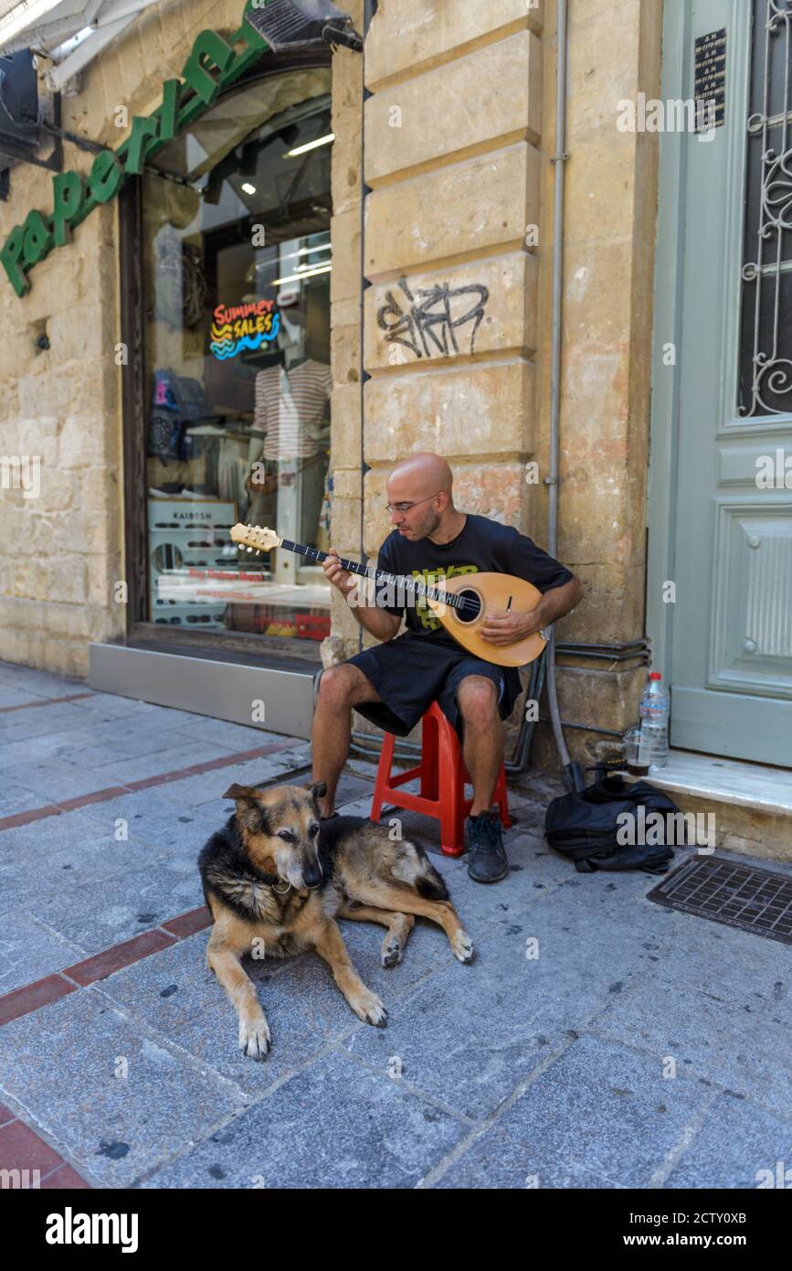 Young man man plays an ancient stringed instrument on the street for Heraklion Greece. His dog is sitting next to him Stock Photo