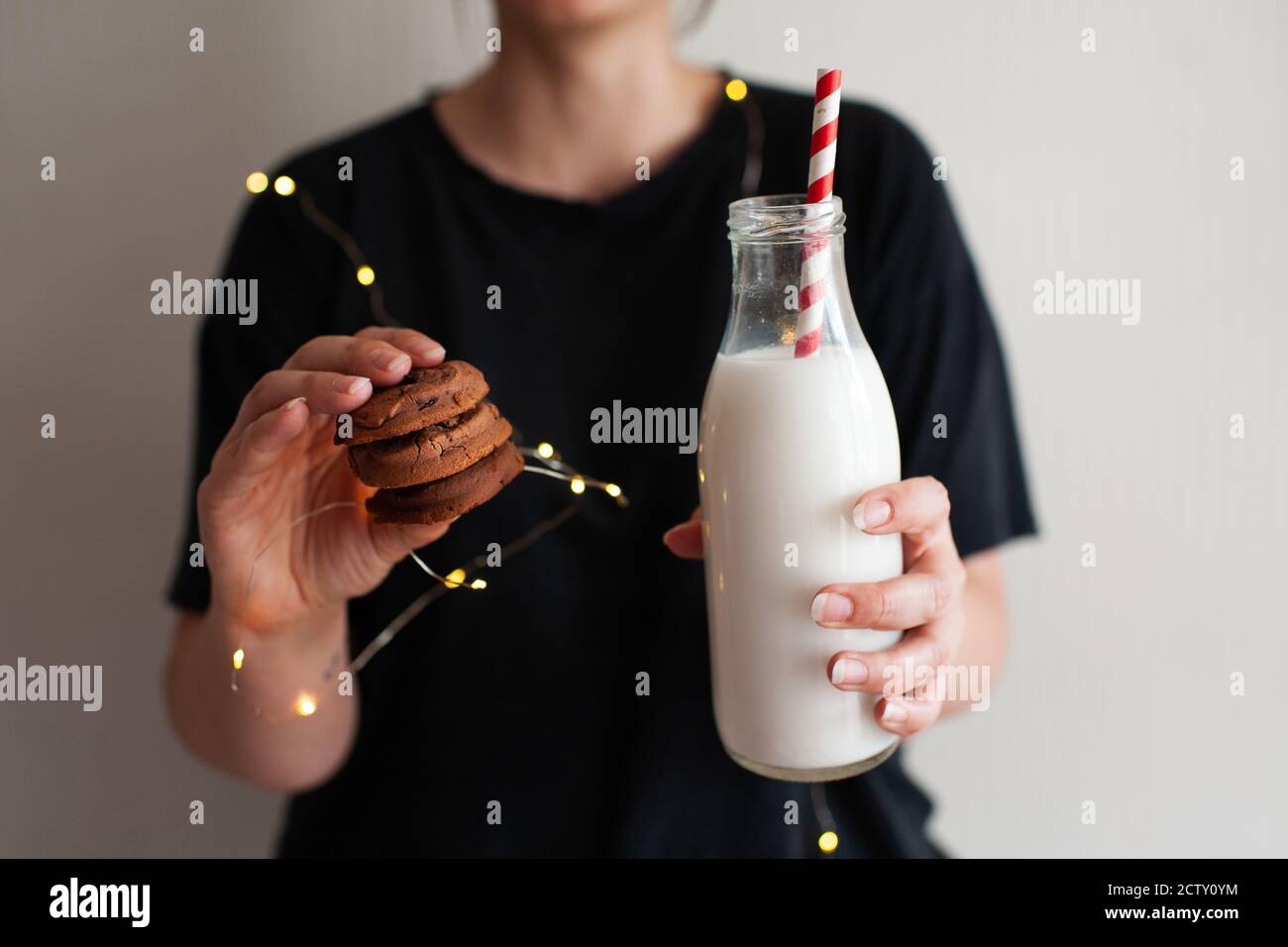Woman holding tasty cookies and bottle of fresh milk over glowing lights close up. Winter holiday season. Good morning. Stock Photo