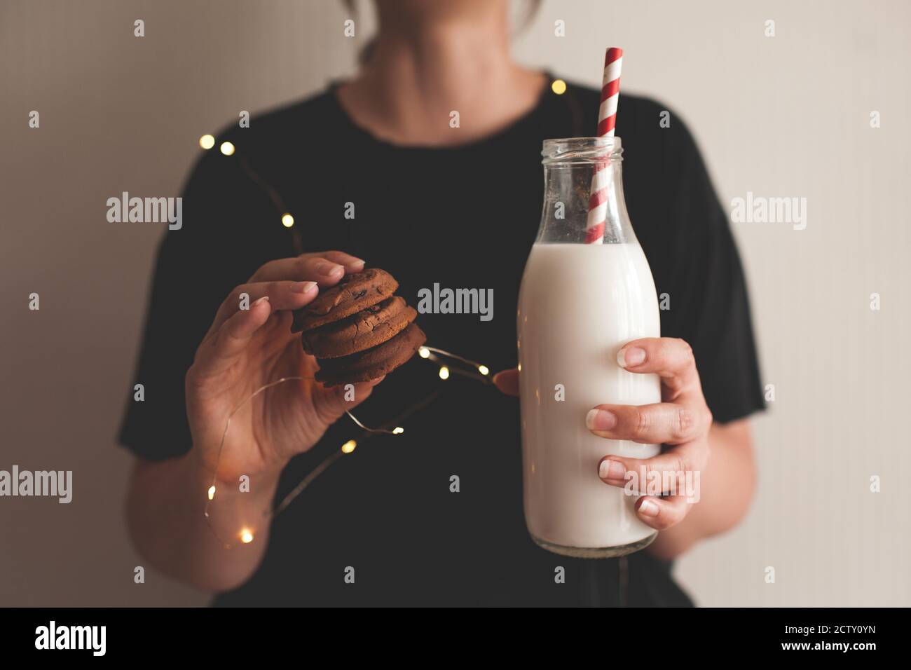 Girl holding chocolate cookies and bottle of fresh milk in room close up. Winter holiday season. Stock Photo