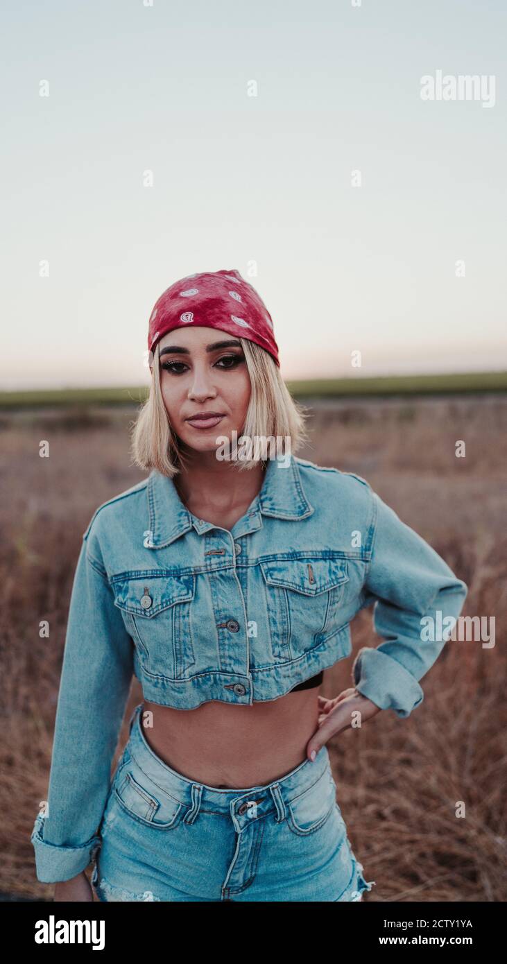 Blonde female wearing a denim outfit paired with a red head bandana and  posing on the road Stock Photo - Alamy