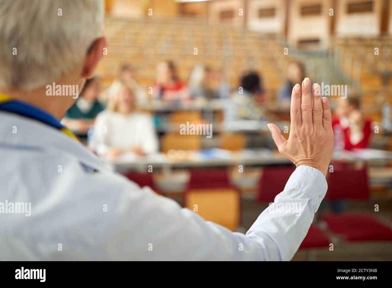 Female professor calming down the students and starting the lecture in the university amphitheater Stock Photo