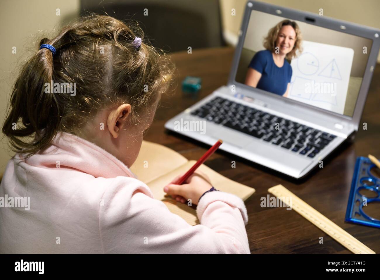Kid virtual learning with teacher by laptop, little girl studies online in room, tutor teaches preschool child during quarantine. Concept of distance Stock Photo