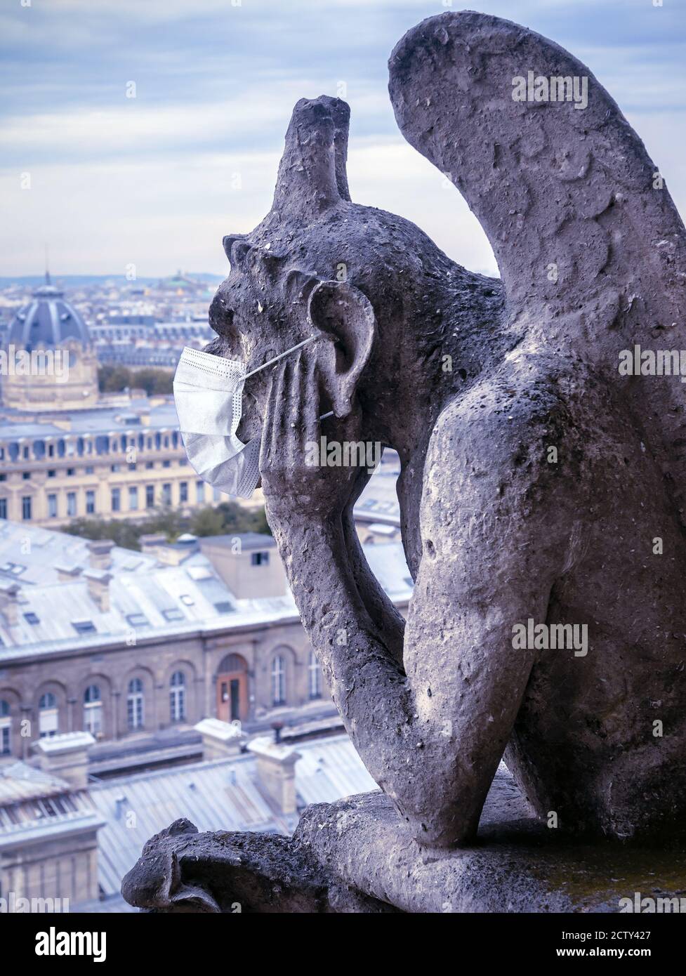COVID-19 coronavirus in France, surgical mask on gargoyle of Notre Dame in Paris. Landmarks closed due to corona virus World pandemic. Concept of trav Stock Photo