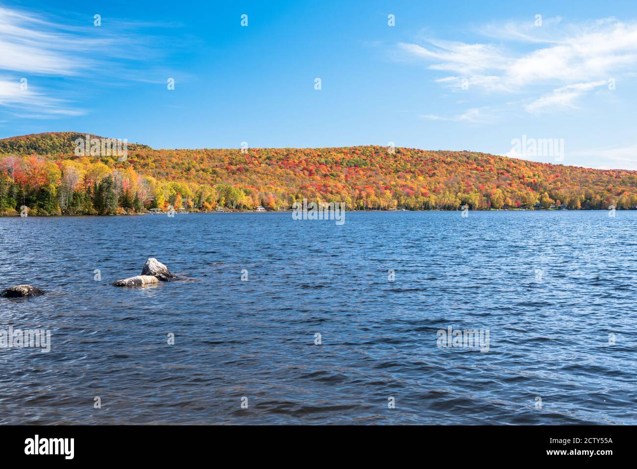 Beautiful mountain lake with forested shores at the peak of autumn colours and blue sky Stock Photo