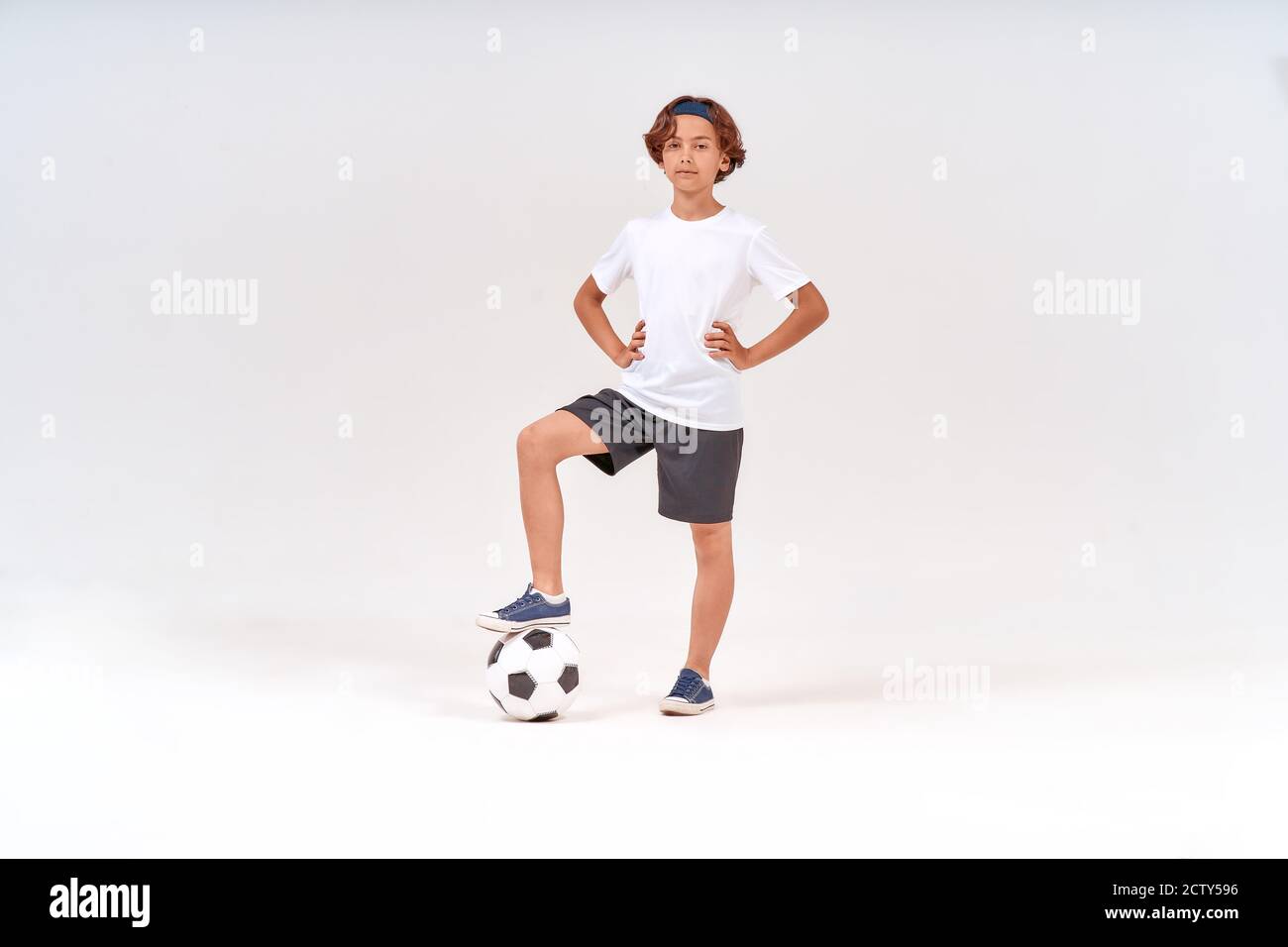 Football player. Full-length shot of a happy teenage boy with soccer ball looking at camera and smiling while standing isolated over grey background Stock Photo