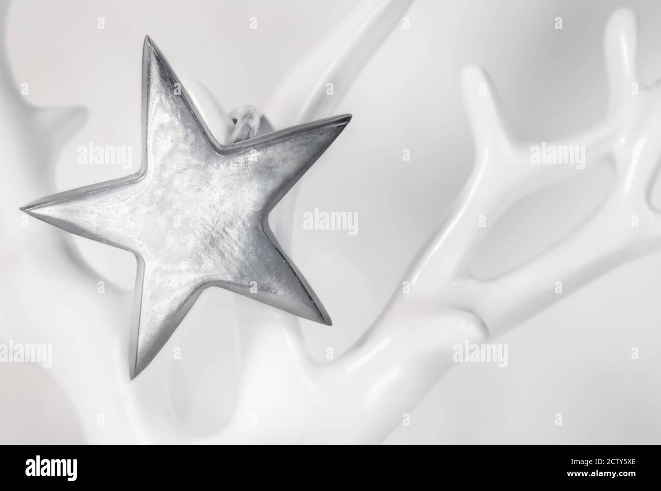 Single silver star on soft white background. Close up. The sterling silver star hangs on a porcelain tree or antler. Stock Photo