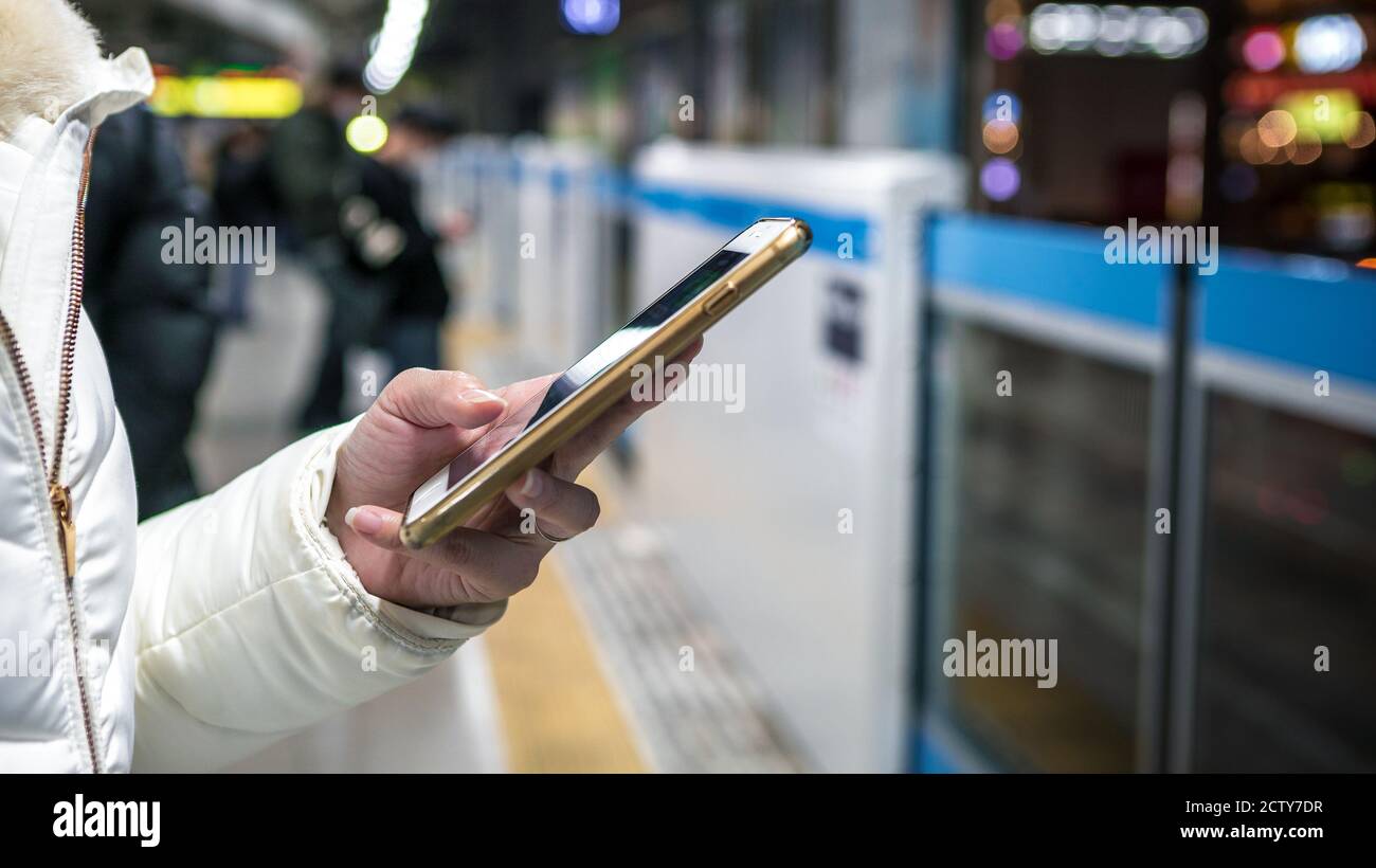 Asian young woman checks her phone in a japanese platform train station. Writing a SMS text using social network. Passenger lifestyle and transportati Stock Photo