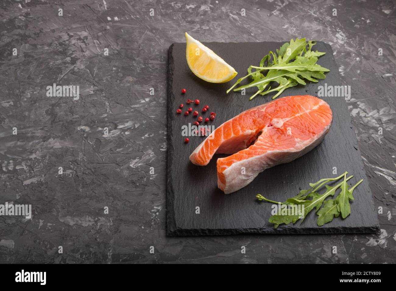 Raw salmon steak with arugula and lemon on a black slate board on a ...