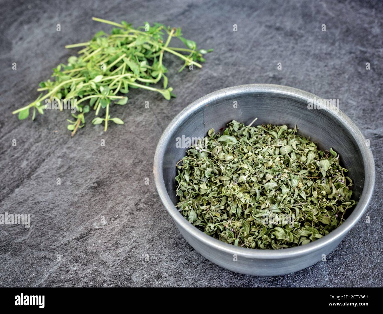 Dried thyme (thymus vulgaris) in metal bowl on dark grey table. Copy space. Stock Photo