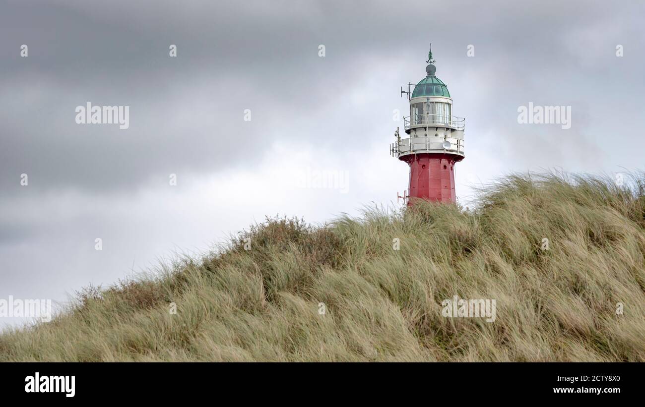 The lighthouse of Scheveningen near the city of the Hague in the Netherlands. The foreground shows a sand dune full of grass and the sky is overcast. Stock Photo