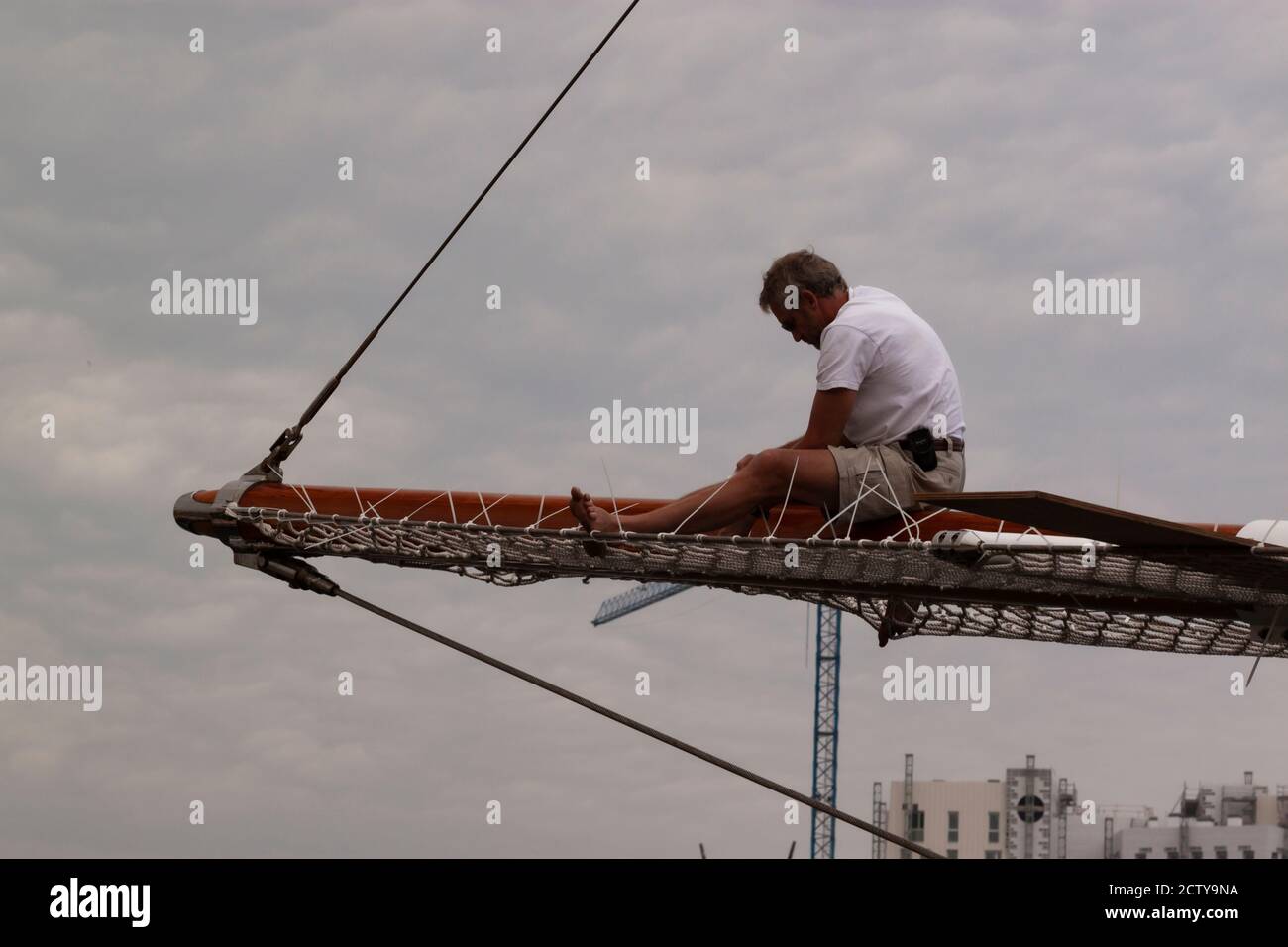 Barcelona, Spain, 05/01/2010: An athletic sailor is sitting on top of the wooden bowsprit of a large vessel trying to fix it. He wears no protective e Stock Photo