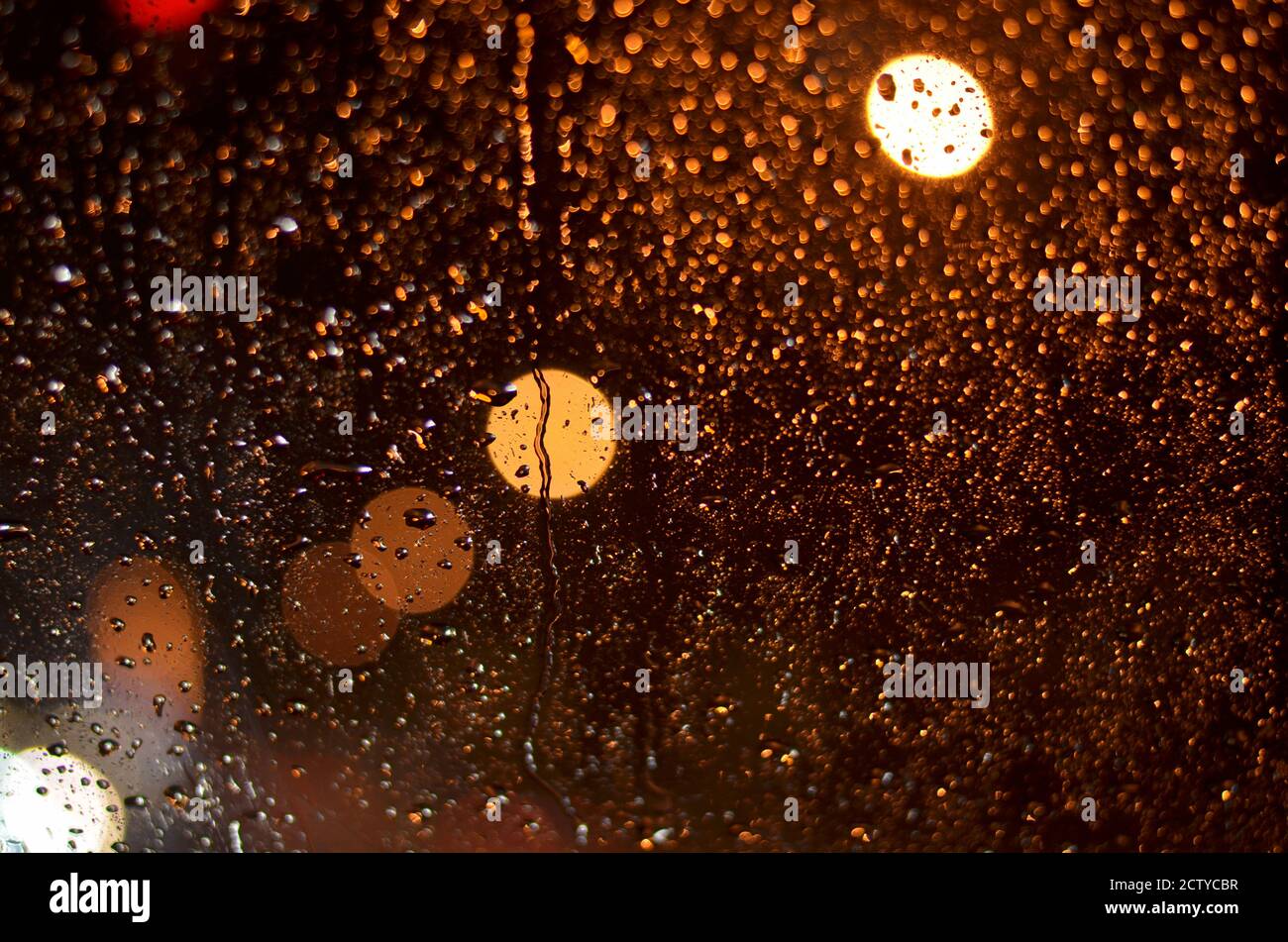Raindrops on the glass of the car lit by street lamps in the night. Stock Photo