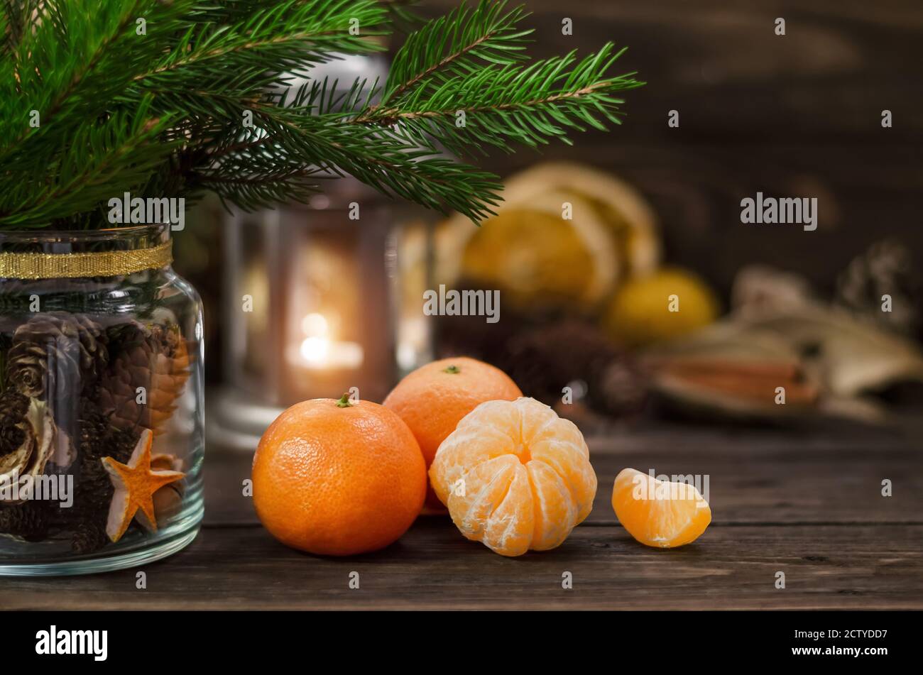 Ripe juicy mandarins, fir twigs and a glass jar with cones close-up on a wooden rustic table. Christmas or New Year holiday concept. Stock Photo