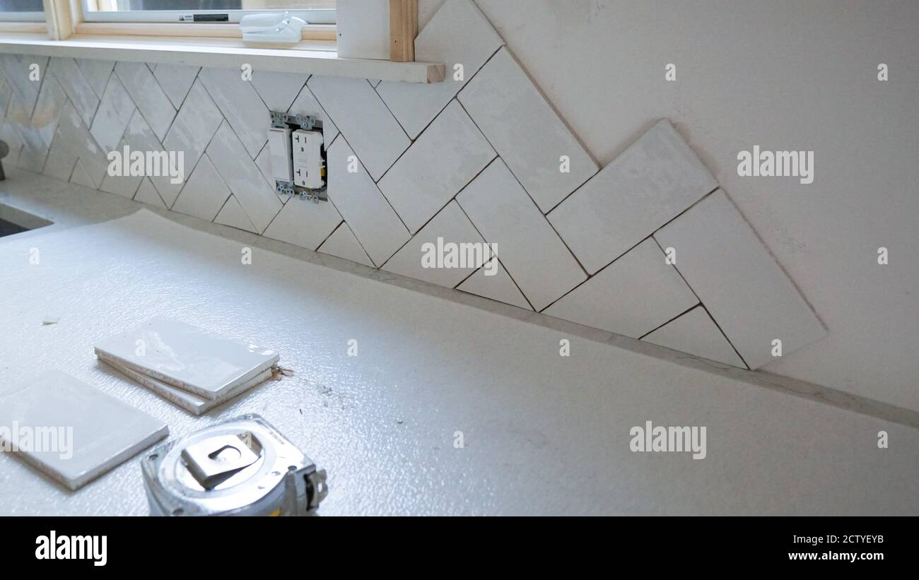 Home improvement project - installing white ceramic tile as a kitchen backsplash. Stock Photo