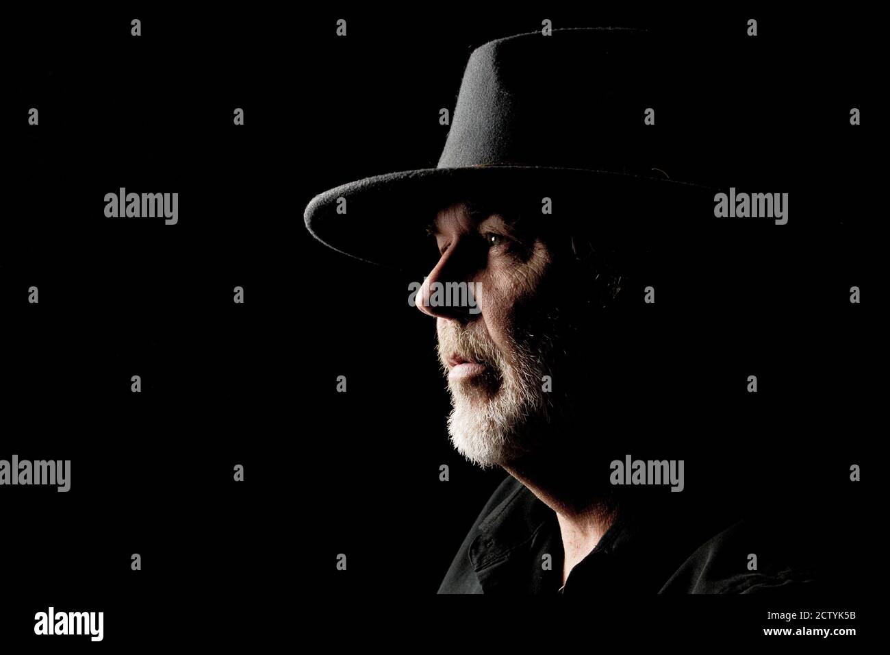 Close-up portrait of bearded middle-aged man in wide-brimmed western hat against a dark background Stock Photo