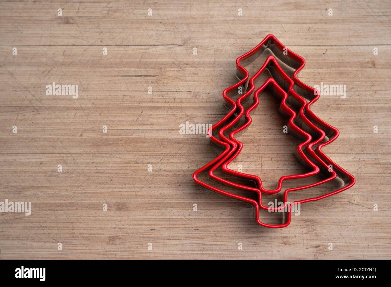 Red Christmas tree cookie cutter on wood cutting board.  Holiday concept. Copy space. Stock Photo