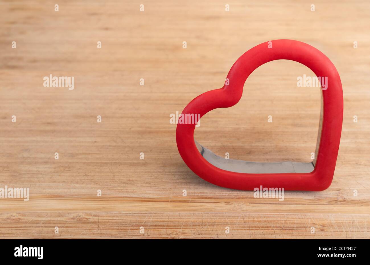 Red heart shaped cookie cutter on wood cutting board. Concept about love. Copy space. Stock Photo
