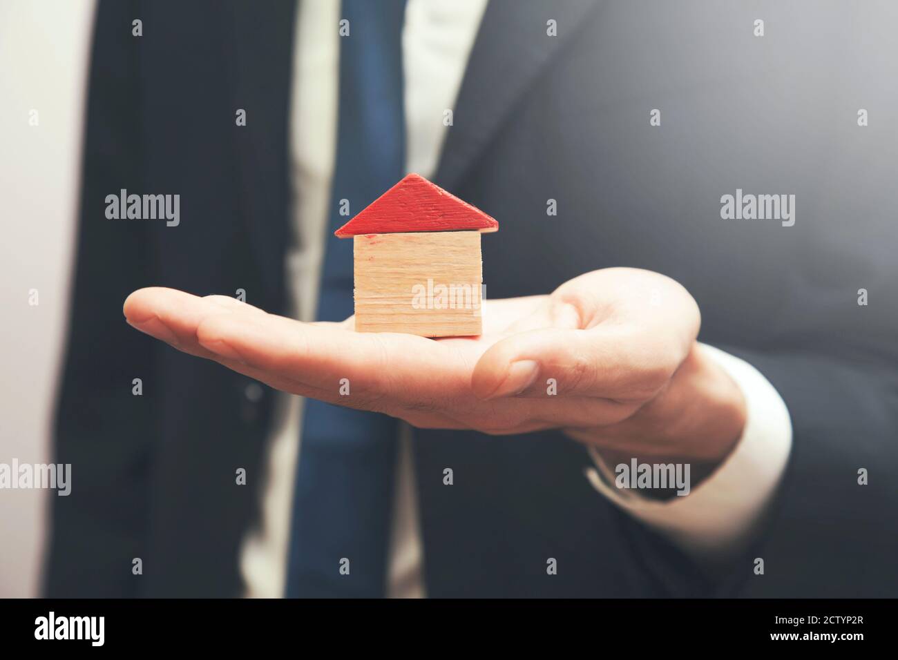 real estate agent holding a wooden house in his hand Stock Photo - Alamy