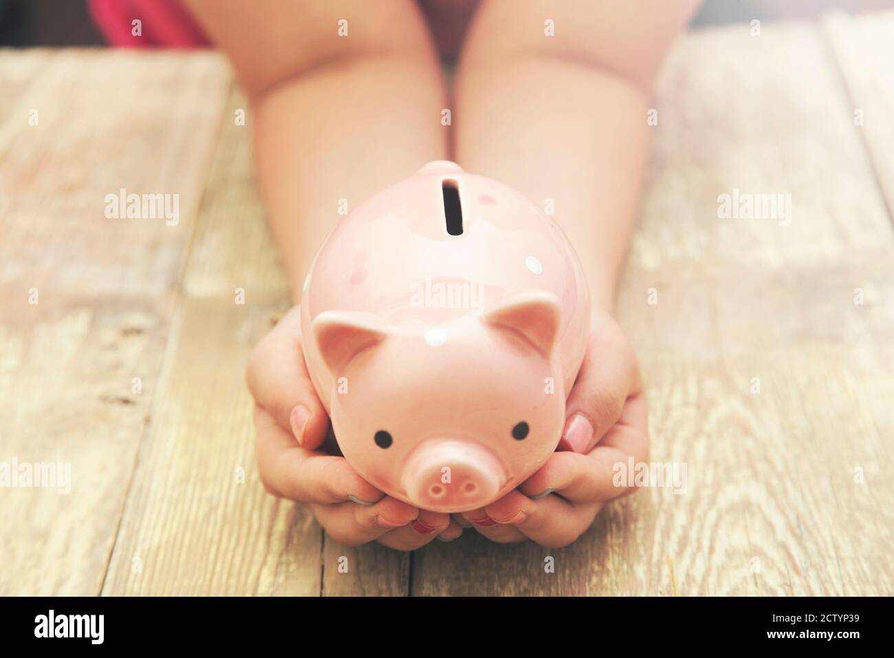 little girl with piggy bank isolated on wooden background Stock Photo