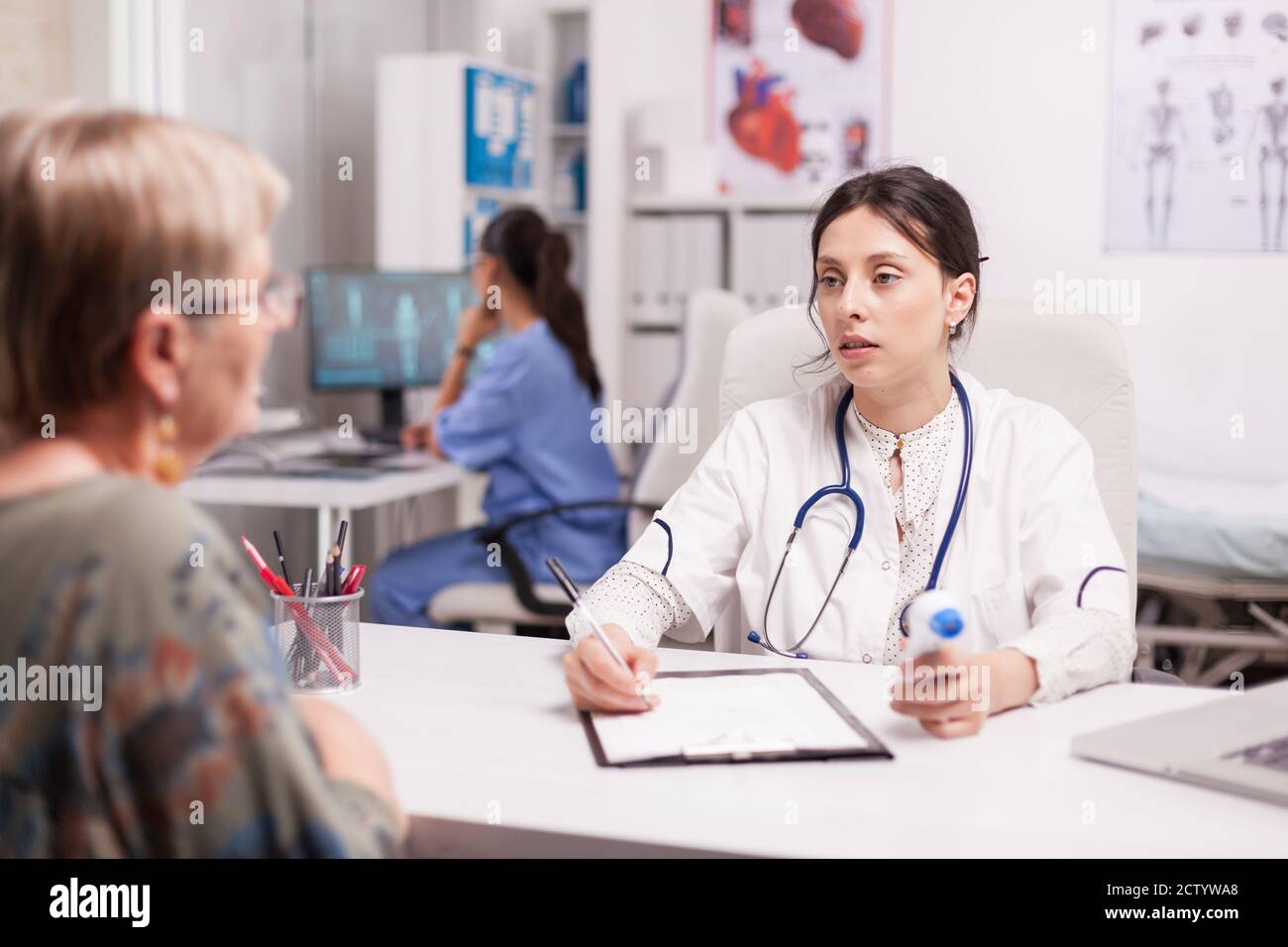 Female doctor looking at senior patient and holding thermometer gun