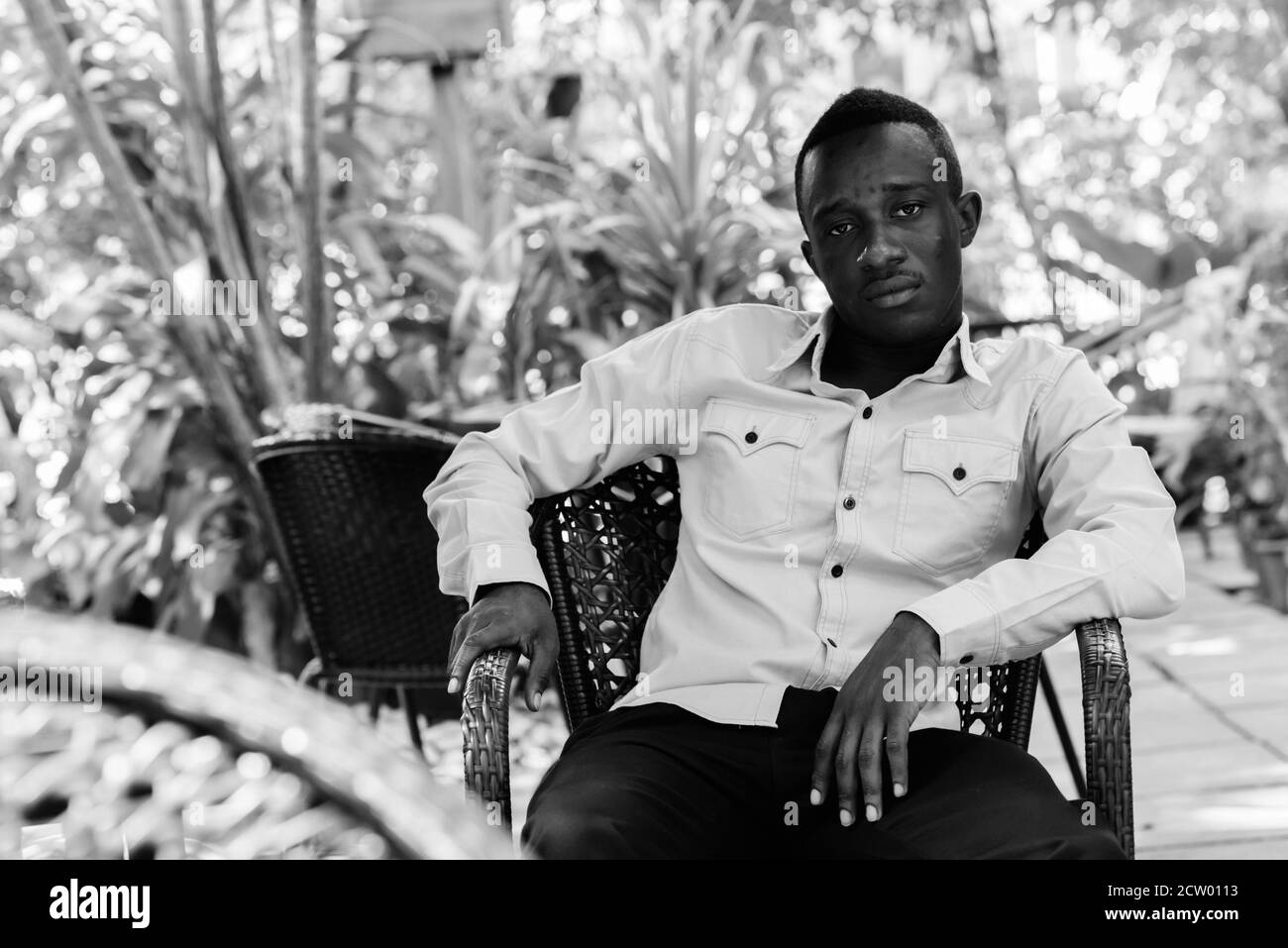 Young black African man sitting at outdoor coffee shop surrounded by nature Stock Photo