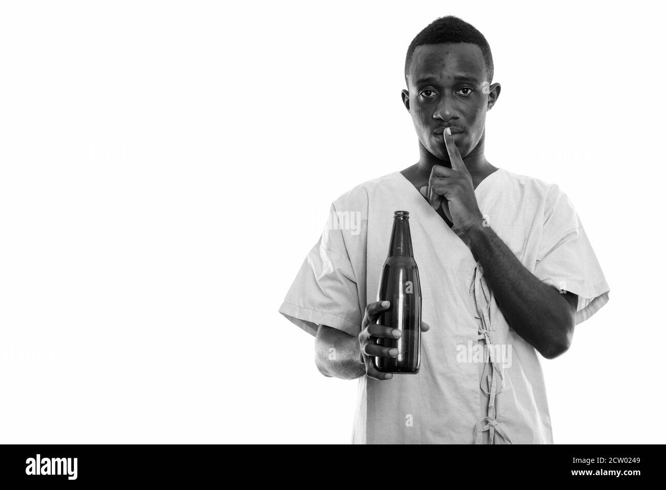 Studio shot of young black African man patient holding bottle of beer with finger on lips Stock Photo