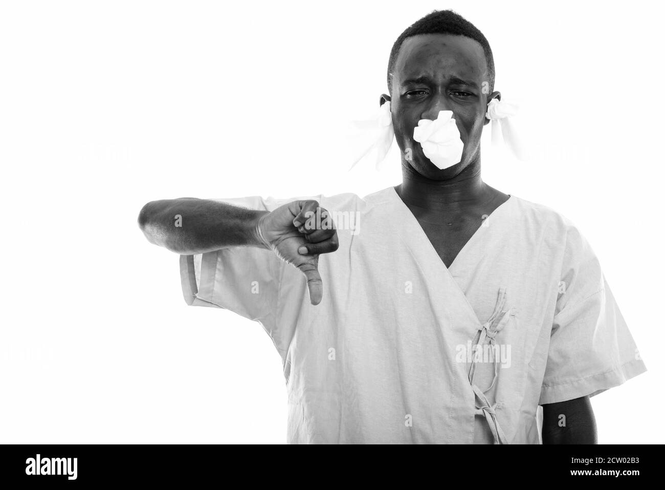 Studio shot of young black African man patient giving thumb down with tissues in his ears and nose Stock Photo