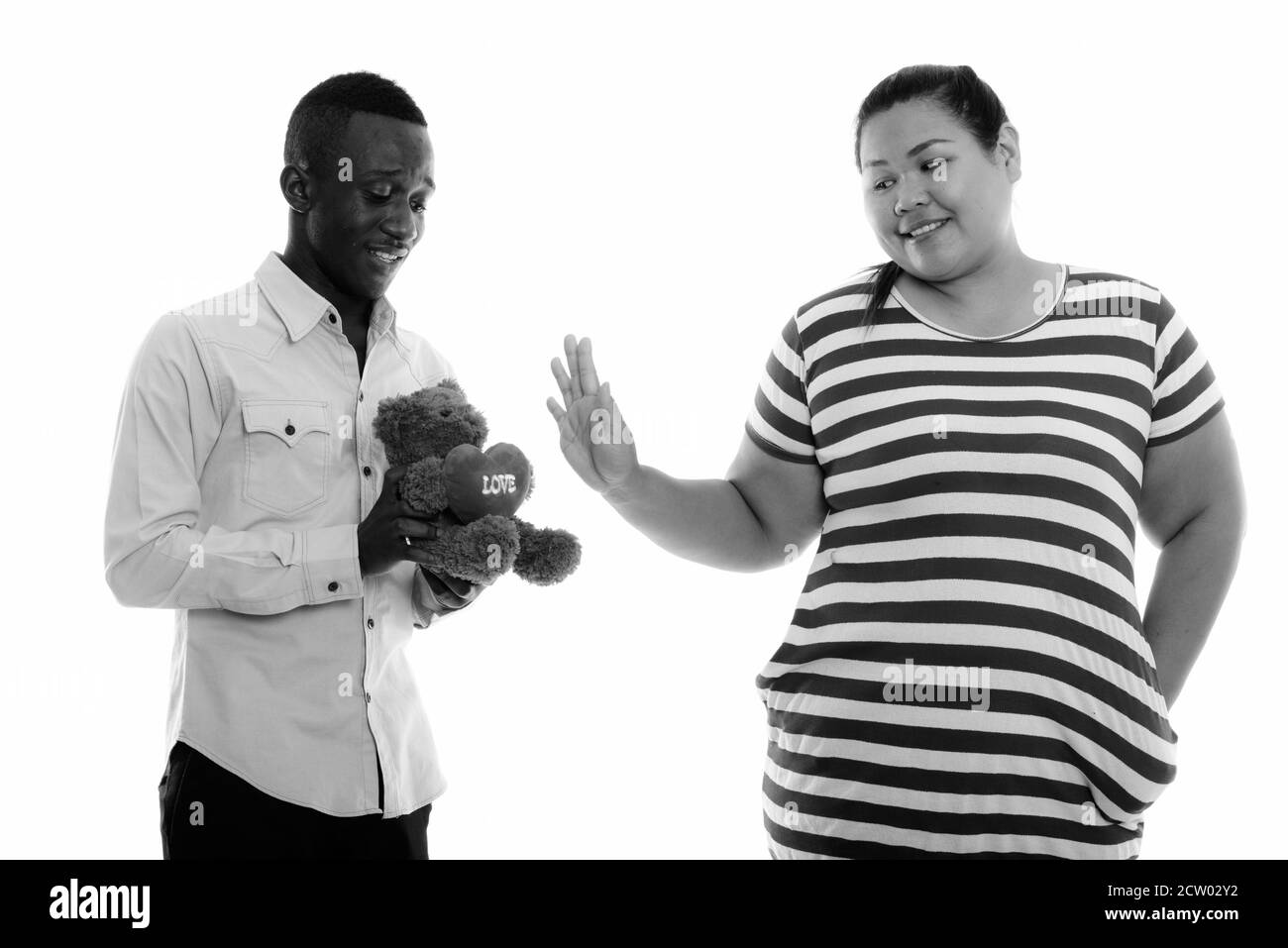 Young overweight Asian woman rejecting young African man with teddy bear Stock Photo