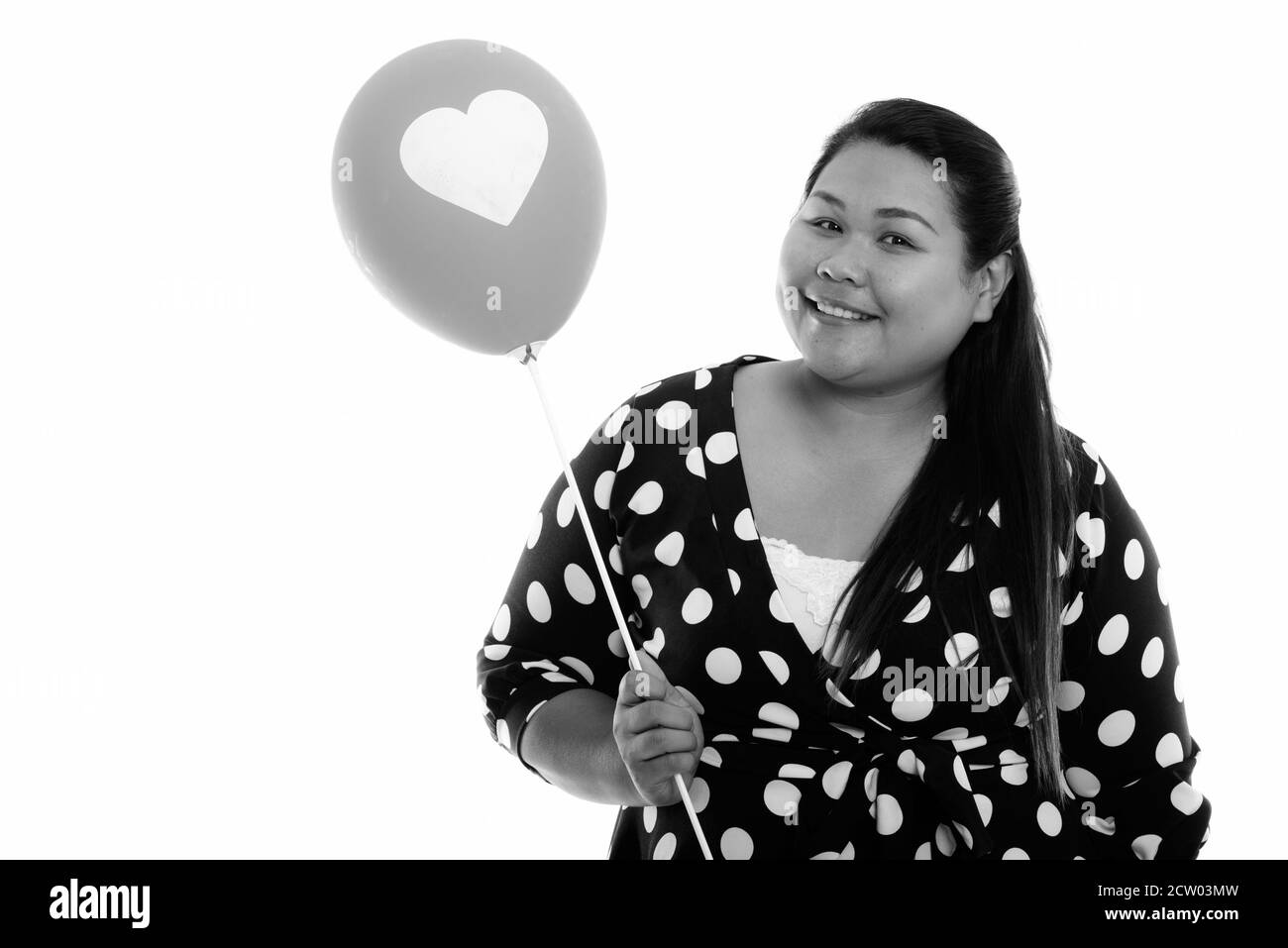 Studio shot of young happy fat Asian woman smiling while holding balloon with heart sign Stock Photo