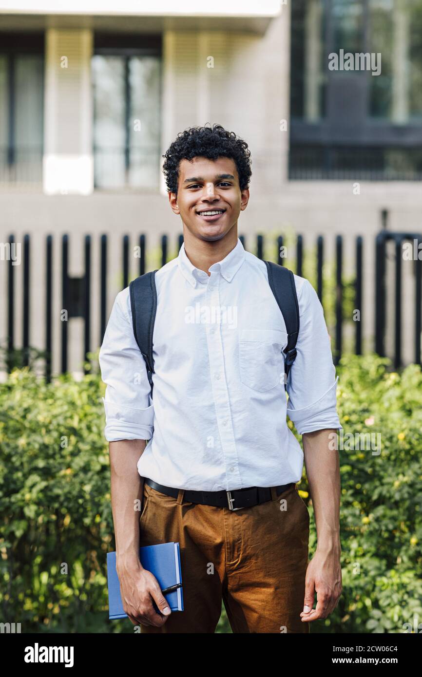 Handsome young man going standing outdoors with backpack and notebook Stock Photo