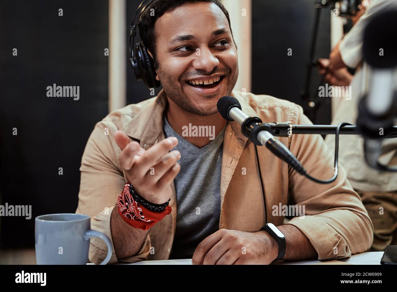 Portrait of happy young male radio host in headphones smiling aside while talking, broadcasting in studio Stock Photo