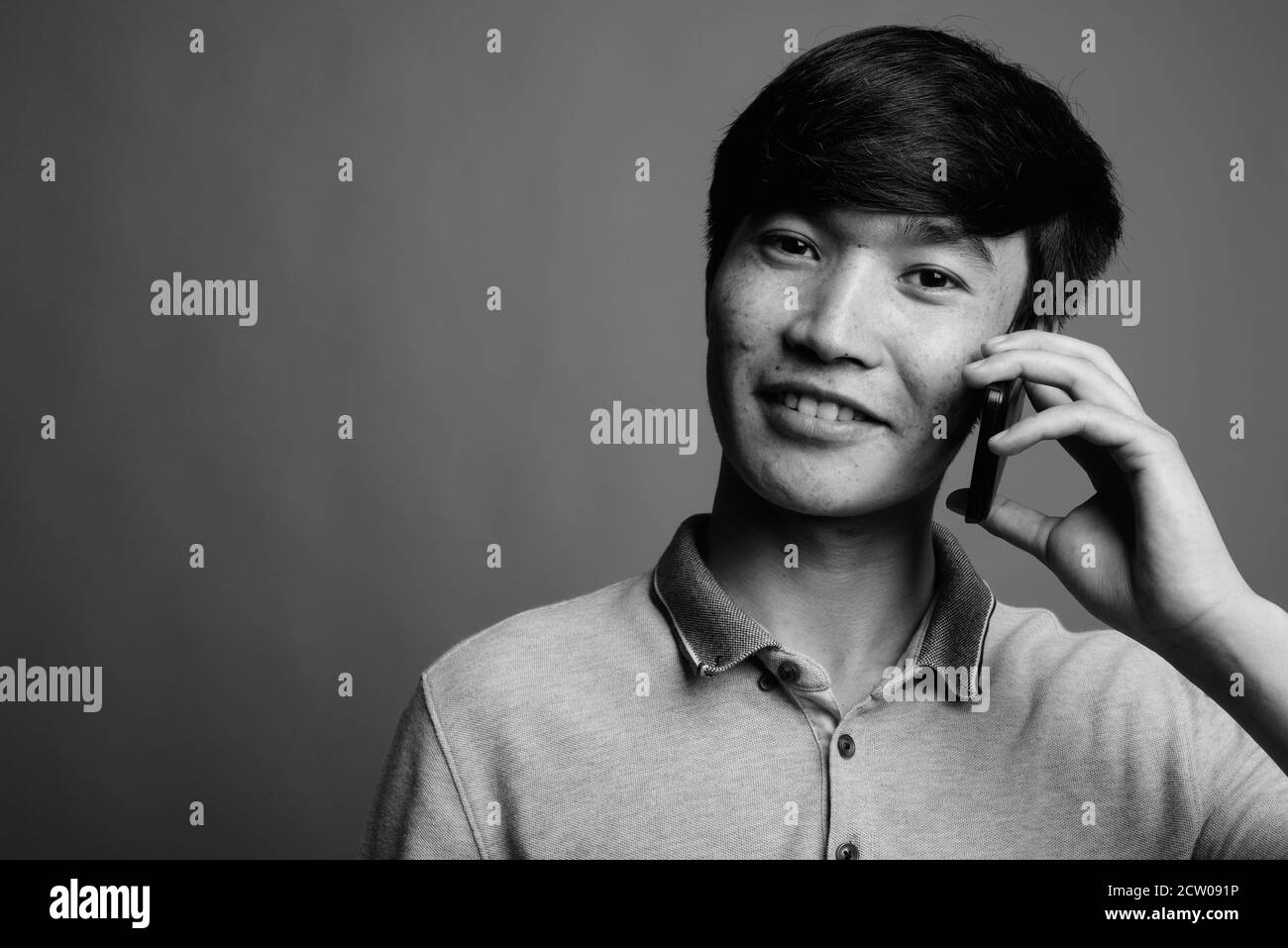 Young Asian man using mobile phone against gray background Stock Photo