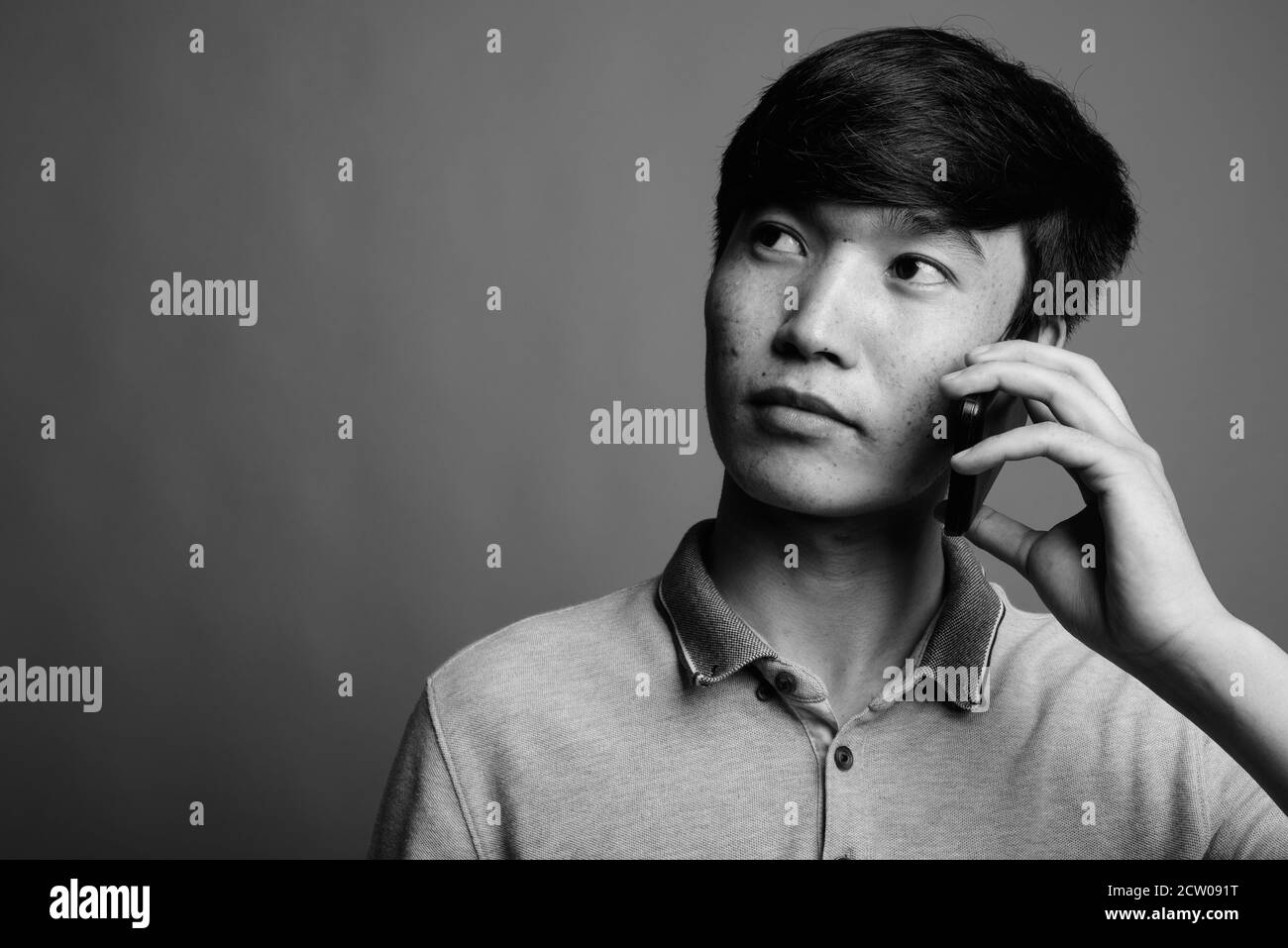 Young Asian man using mobile phone against gray background Stock Photo