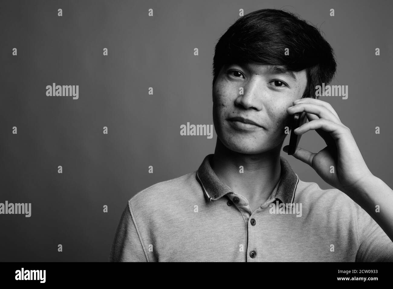 Young Asian man using mobile phone against gray background Stock Photo