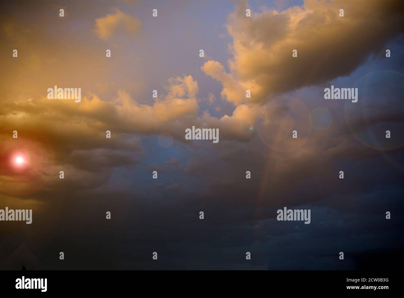 Orange stormy sunset with a clouds with a lens flare Stock Photo - Alamy