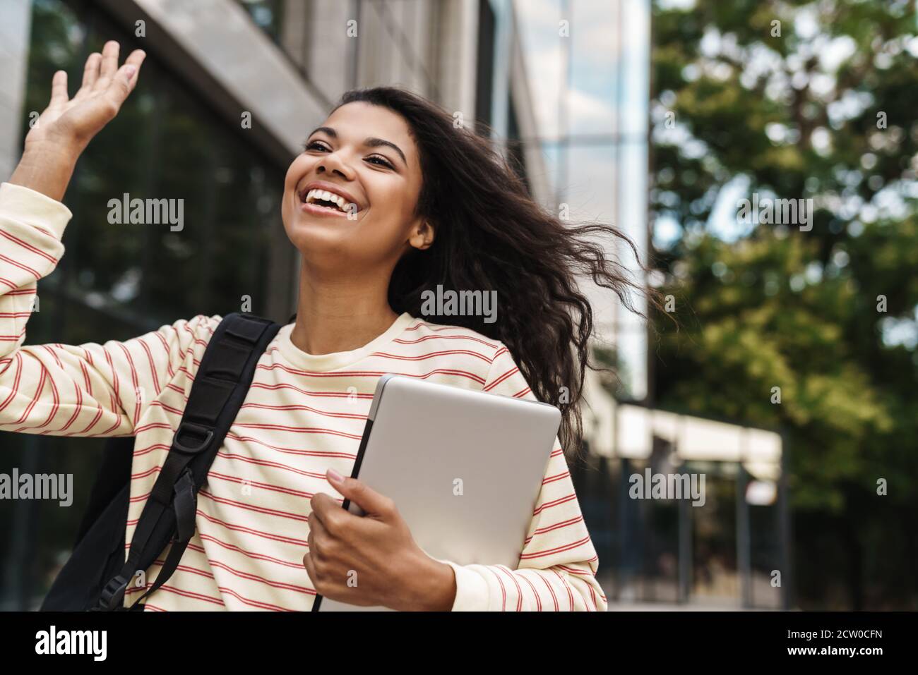 Image of smiling african american girl waving hand and holding laptop ...