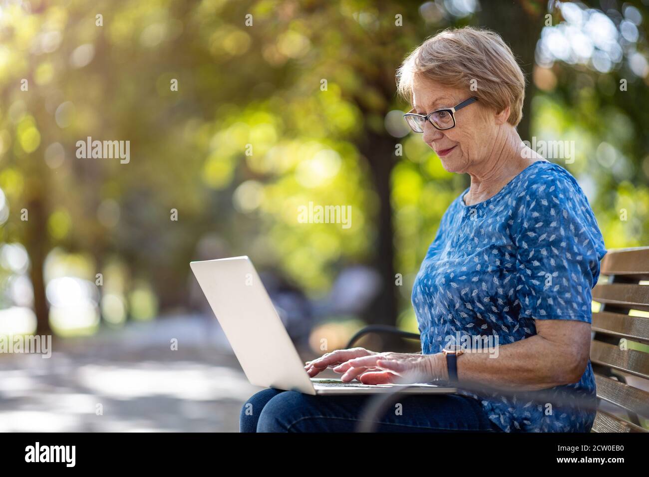Senior woman using laptop on bench outdoors Stock Photo